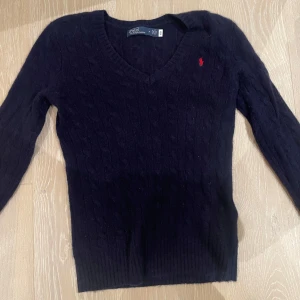 Svart tröja från Ralph Lauren - Säljer en snygg svart tröja från Ralph Lauren med v-ringning och det klassiska röda logotypen på bröstet. Tröjan är i bra skick och har långa ärmar, perfekt för höst och vinter. Passar både till vardags och lite finare tillfällen. Använd 1 gång⭐️