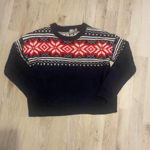 Mönstrad stickad tröja från ASOS - Säljer en superfin stickad tröja från ASOS i storlek 36. Den är mörkblå med ett snyggt rött och vitt mönster över bröstet. Perfekt för kalla dagar. Tröjan har långa ärmar och är i mycket bra skick. Passar perfekt till både vardag och julen!