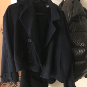 Mörkblå kappa - Säljer en snygg mörkblå kappa i bra skick. Den har en klassisk design med stora knappar framtill och en stilren krage. Perfekt för höst och vår, och funkar både till vardags och lite finare tillfällen. Passar bra över en tröja eller skjorta.