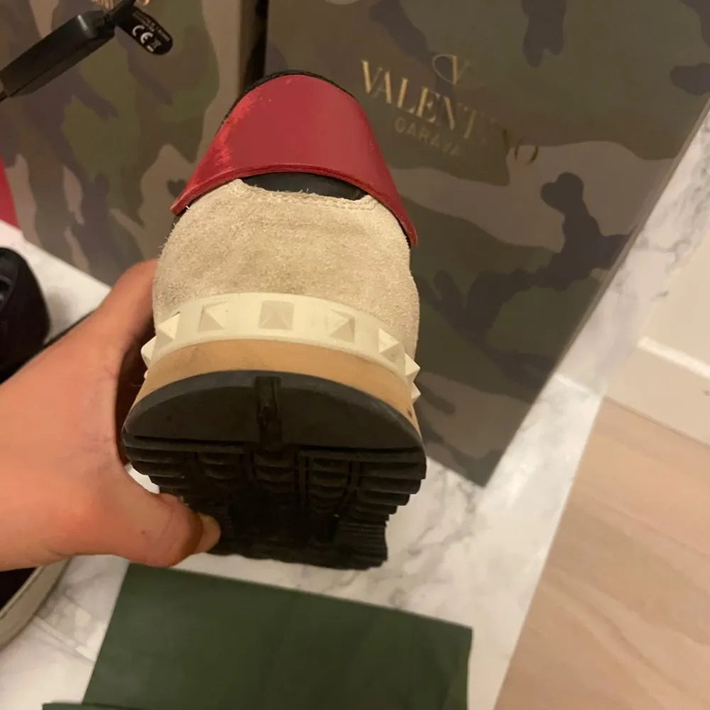 Säljer ett par snygga Valentino Rockrunner sneakers i camouflage. Skorna har en cool mix av gröna, röda och beige toner med mocka- och skinnmaterial. De har snörning och en unik nitar-detalj på hälen. Perfekta för en trendig look!. Skor.