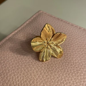 Guld ring blomma - Snygg guldfärgad ring formad som en blomma. Den har detaljerade blomblad och en justerbar ringdel för perfekt passform. Perfekt accessoar för att ge en touch av elegans till vilken outfit som helst. Passar både till vardags och festliga tillfällen. Helt ny!