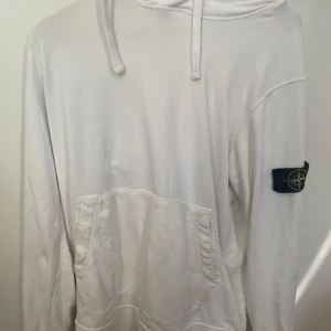 Vit hoodie från Stone Island - Säljer en stilren vit hoodie från Stone Island. Den har en klassisk känguruficka och den ikoniska loggan på ärmen. Perfekt för både vardag och chill. Passar bra till jeans eller joggers. Hör av dig vid intresse!