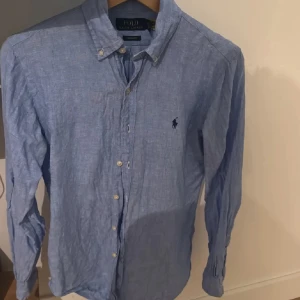 Blå skjorta från Ralph Lauren - Säljer en snygg blå skjorta från Ralph Lauren i bomull. Den har en klassisk krage och knappar hela vägen ner. Perfekt för både vardag och fest! Skjortan är i mycket bra skick och har långa ärmar. Den ikoniska loggan är broderad på bröstet. Passar perfekt till jeans eller chinos.