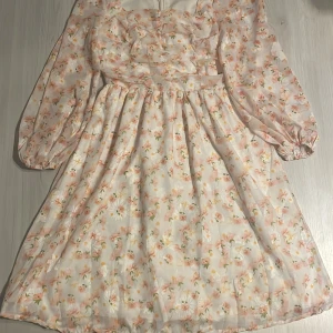 Blommig klänning  - Säljer en superfin blommig klänning i storlek S. Den har långa ärmar och en dragkedja i ryggen. Perfekt för vår och sommar med sitt ljusa, blommiga mönster. Klänningen är i mycket bra skick och bara använd en gång. 