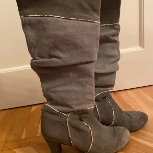 Grå stövlar med klack - Säljer ett par snygga grå stövlar i mocka med klack. De har en cool design med ljusa sömmar som ger en extra touch. Perfekta för höst och vinter, och de passar både till vardags och fest. Stövlarna är i bra skick och redo för nya äventyr! Är i storlek 39 men är något små för mig som normalt bär 39