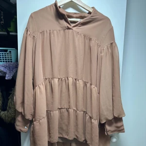 Beige långärmad klänning - Säljer en superfin beige klänning med långa ärmar och en loose passform. Den har en volangdetalj som ger en extra touch av stil. Perfekt för höst och vår, och kan stylas både upp och ner beroende på tillfälle. Materialet känns mjukt och bekvämt mot huden.