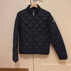 Svart quiltad jacka | GANT - Säljer en snygg svart quiltad jacka från GANT i mycket bra skick om man bortser från lagningen(som inte syns).Se bild 5 . Den har en dragkedja framtill och ett stilrent märke på ärmen. Perfekt för höst och vår, med en klassisk look som funkar till det mesta. Passar ungdomar runt 15 år.