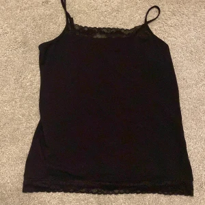 Svart linne med spetsdetaljer från Lindex - Säljer ett svart linne från Lindex i storlek EUR 170. Det har smala axelband och fina spetsdetaljer vid halsringningen och nederkanten. Perfekt som det är. Använd några gånger men i mycket bra skick!