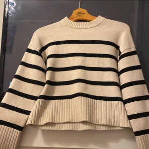 Randig stickad tröja - Säljer en superfin randig tröja i beige och svart. Den är stickad och perfekt för höst och vinter. Tröjan har långa ärmar och ribbade muddar vid ärmslut och nederkant. 