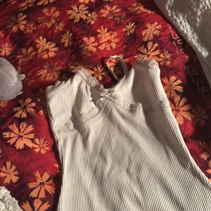 Vit ribbad klängig med spetsdetaljer - Säljer en superfin vit ribbad klänning från hm divided i storlek XS. Den har vackra spetsdetaljer vid halsringningen och axelbanden, samt en söt liten rosett framtill. Perfekt för sommardagar eller som ett lager under en tröja. 🕊️