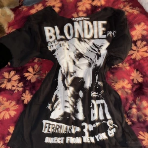 Svart Blondie t-shirt - Cool svart t-shirt med stort tryck av Blondie på framsidan. Den har ett vintage-inspirerat motiv med texten '1977' och 'Direct from New York City'. Perfekt för dig som älskar retro och musik! Passar till både vardag och konsert.