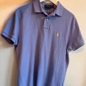 Ljusblå pikétröja från Ralph Lauren - Säljer en stilren ljusblå pikétröja från Ralph Lauren. Den har korta ärmar och en klassisk krage med två knappar. Perfekt för både vardag och lite finare tillfällen. Den ikoniska loggan är broderad på bröstet. Passar perfekt till jeans eller chinos!