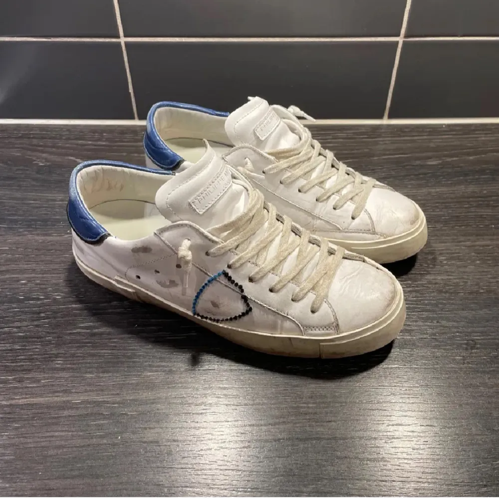 Säljer ett par vita sneakers från Philippe Model i bra skick. De har blå detaljer på hälen och klassisk snörning. Skorna kommer med originalförpackning och påse. Storleken är 40-41. Skor.