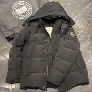 Svart vinterjacka från Canada Goose black label.  - Säljer en svart vinter jacka från Canada Goose i nytt och  bra skick. Jackan är perfekt för vintern med sin tjocka vaddering och långa ärmar. Den har en dragkedja och knappar framtill samt en avtagbar huva. Märkets logga syns på ärmen och päls följer med. Perfekt för kalla dagar! ❄️