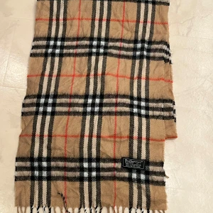 Rutig halsduk från Burberry - Säljer en klassisk rutig halsduk från Burberry i 100% kashmir. Den är i beige med svarta, vita och röda rutor. Perfekt för att hålla dig varm och stilren under höst och vinter. Halsduken är i mycket bra skick och supermjuk. Passar både till vardags och fest! 🧣✨Priset kan diskuteras!