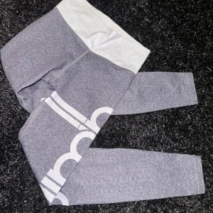 Grå leggings från Aim’n - Säljer ett par grå leggings från Aim’n i storlek XS, passar S då de är töjbara. De är i mycket bra skick och har en snygg vit logga längs benet. Perfekta för träning eller en avslappnad dag. Materialet är mjukt och stretchigt för bästa komfort.