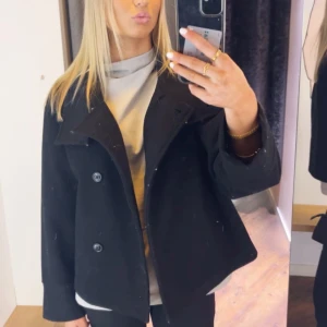 Svart kappa - Säljer en stilren svart kappa i mycket bra skick. Den har en klassisk design med knappar framtill och en lös passform. Perfekt för höst och vår, och funkar både till vardags och fest. Storleken är dam S-M