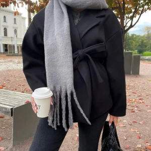 Svart kappa med knytband - Säljer en stilren svart kappa med knytband i midjan. Perfekt för höst och vår, med en elegant omlott-design och långa ärmar. Jackan har en klassisk look som passar både till vardags och fest. Superfin att matcha med en stor halsduk och jeans! Väldigt fint skick!💓