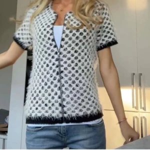 Svartvit kofta med prickar - Säljer en fluffig och mysig svartvit kofta med korta ärmar och dragkedja. Den har ett unikt mönster och är perfekt för både vardag och fest. Passar bra till jeans eller kjol för en stilren look.