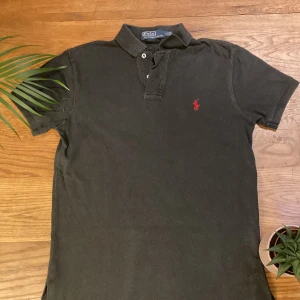 Svart pikétröja från Ralph Lauren - Säljer en klassisk svart pikétröja från Ralph Lauren i storlek S. Tröjan har en broderad röd logga på bröstet och är i bomull. Perfekt för både vardag och fest! Den är i bra skick och har en normal passform.