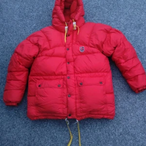 Röd dunjacka från Fjällräven - Säljer en supervarm och snygg röd dunjacka från Fjällräven, det är den gammal och tjocka modellen i storlek xxs. Perfekt för kalla vinterdagar! Jackan har en justerbar huva med gula snören och praktiska fickor framtill. Den är i mycket bra skick, men har dock två små svarta fläckar som säkert går bort vid kemtvätt💕💕