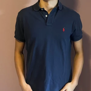 Mörkblå pikétröja från Ralph Lauren - Säljer en snygg mörkblå pikétröja från Ralph Lauren i bra skick. Den har en klassisk krage och korta ärmar, perfekt för både vardag och fest. Pris kan diskuteras vid snabb affär. Hör av dig vid minsta fråga!