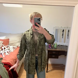 Grön blommig jacka/overshirt med knytband - Säljer en superfin grön jacka/skjorta med blommigt mönster. Den har knytband i midjan och långa ärmar. Perfekt för vår och höst! Jackan är i bra skick och passar till både vardag och fest. 
