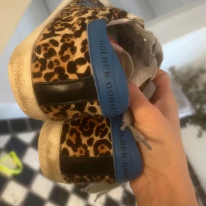 Leopardmönstrade sneakers från Golden Goose - Säljer ett par coola leopardmönstrade sneakers från Golden Goose. De har en vintage-look med slitna detaljer och texten 'FOR DREAMERS USE ONLY' på sidan. Skorna har blå och svarta detaljer samt snörning. Perfekta för att ge din outfit en unik touch!