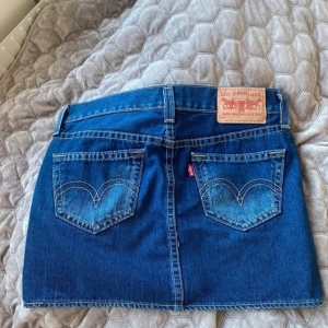 Jeanskjol från Levi's - Säljer en snygg jeanskjol från Levi's i storlek L. Kjolen är i klassisk blå denim med fem fickor och en bekväm passform. Perfekt för både vardag och fest! Tillverkad av 84% bomull och 16% polyester, vilket ger en skön och hållbar känsla. Levi's logga syns tydligt på baksidan. 🕶️👖