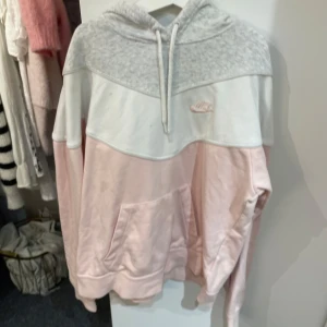 Grå och rosa hoodie från Nike - Säljer en supermysig hoodie från Nike i storlek S. Den har en snygg färgblockdesign med grått upptill och ljusrosa nedtill. Perfekt för kyliga dagar med sin mjuka och bekväma passform. Den har en klassisk känguruficka och justerbar huva. Perfekt för både vardag och träning! Den har några fläckar men dom syns knappt!🌸
