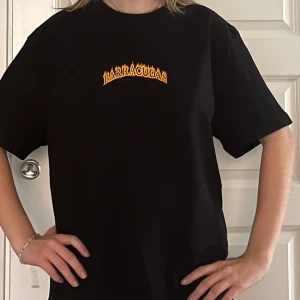 Svart t-shirt med Barracudas-tryck - Säljer en svart t-shirt med coolt Barracudas-tryck i orange och gult på bröstet. Från Weekday och endast använd ett fåtal gånger. Perfekt oversized fits