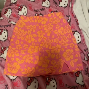 Blommig kortkjol från BikBok - Säljer en superfin kortkjol från BikBok i storlek XS. Kjolen är rosa med ett härligt gult blommönster och har en liten slits framtill. Perfekt för sommardagar eller en festlig kväll! 🌸