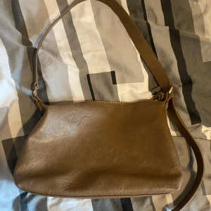 Brun axelväska från Fashion & Bags - Så snygg brun axelväska som tyvärr inte kommer till användning längre. Väskan är i läderimitation. Perfekt för vardagsbruk och är väldigt rymlig. Remmen är justerbar för bästa passform. Obs! Fick sy dragkedjan (se sista bild) men är inte något som syns så mycket!