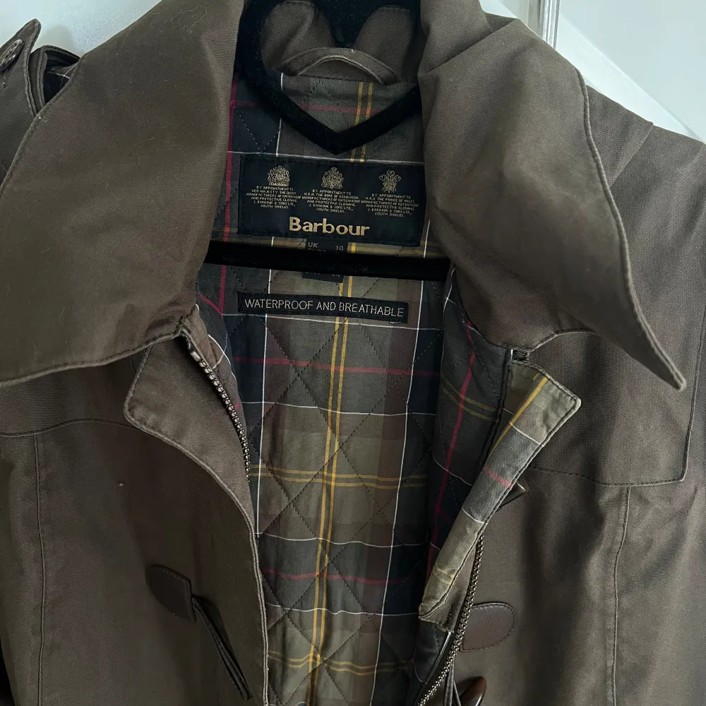 Säljer en snygg brun jacka från Barbour. Den är vattentät och andas, perfekt för höst och vår. Jackan har en klassisk design med knappar och en avtagbar huva. Insidan har ett stilrent rutigt mönster, jackan är lätt figur sydd. Den är i storlek 40 och passar perfekt för en stilren look. Oanvänd . Jackor.