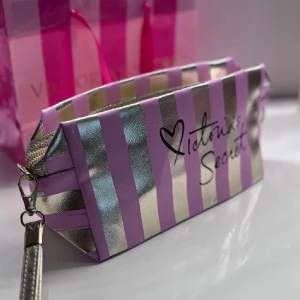 Randig necessär från Victoria's Secret - Säljer en superfin necessär från Victoria's Secret med rosa och silverfärgade ränder. Den har en praktisk dragkedja och är perfekt för att förvara smink eller andra småsaker. Perfekt för resor eller som en söt accessoar i badrummet!