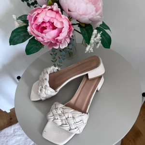 Vita flätade sandaler med klack - Säljer ett par snygga vita sandaler med en flätad design över foten. De har en låg klack som gör dem bekväma att gå i, perfekt för sommarens alla fester. Sandalerna har en fyrkantig tå. Superfina att matcha med både klänning och jeans!