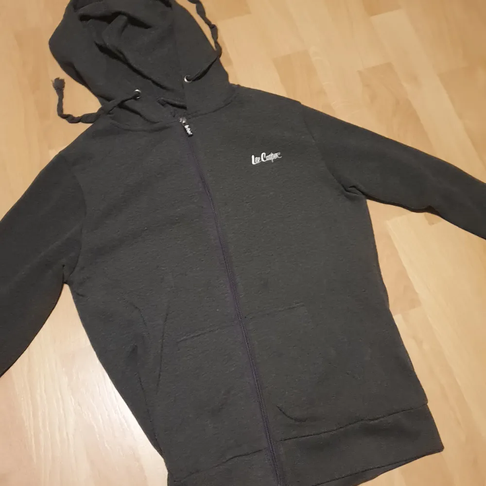 Säljer en snygg svart hoodie från Lee Cooper. Den har en dragkedja framtill och en justerbar huva med snören. Perfekt för en avslappnad stil och passar bra till både jeans och träningsbyxor. Använd ett fåtal gånger, så den är i bra skick!. Tröjor & Koftor.