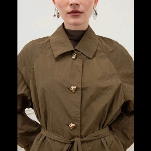 Brun trenchcoat från Missguided - Säljer en snygg brun trenchcoat från Missguided. Den har en klassisk design med knappar och ett bälte i midjan för en perfekt passform. Jackan är lång och har långa ärmar, vilket gör den perfekt för höst och vår. Materialet ser ut att vara lätt och bekvämt. Köpt för 899kr, säljer för endast 449kr!