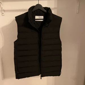 Svart dunväst från Selected - Säljer en snygg svart dunväst från Selected Homme. Perfekt för lager på lager under höst och vår. Västen är i nyskick och passar både till vardags och lite mer uppklädda tillfällen.