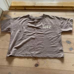 Säljer en brun t-shirt från Lindex med texten 'do what you love' tryckt på framsidan. T-shirten är kortärmad och är lite croppad. Perfekt för en avslappnad stil!