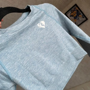 Ljusblå croppad tröja från Women's Best - Säljer en superfin ljusblå croppad tröja från Women's Best. Den är perfekt för träning eller en chill dag. Tröjan är långärmad och har en liten logga på bröstet. Materialet är en mix av nylon, polyester och elastan vilket gör den både bekväm och stretchig. Perfekt för gymmet eller en aktiv dag! Passar både XS/S.