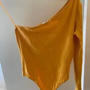 Säljer en snygg gul/orange oneshoulder body från NAKD. Perfekt för en somrig look eller en utekväll. Toppen är i ett mjukt material och har en tight passform. Använd ett par gånger men i bra skick!