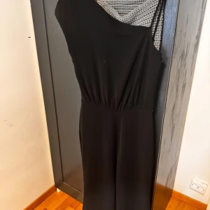 Svart oneshoulder klänning från Zara - Säljer en elegant svart oneshoulder klänning från Zara. Den har en tight passform som framhäver figuren och är perfekt för festliga tillfällen. Klänningen är i nyskick och har en stilren design som passar både till vardags och fest.