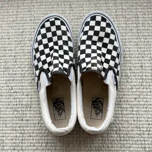 Säljer ett par klassiska svartvita slip-on sneakers från Vans med det ikoniska rutiga mönstret. Skorna är i bra skick och perfekta för en avslappnad stil. De har en bekväm passform och är lätta att ta på och av.