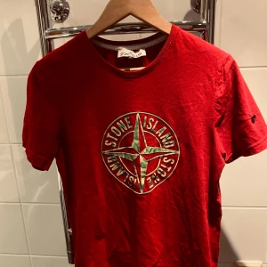 Röd t-shirt från Stone Island - Säljer en röd t-shirt från Stone Island i storlek M. Den har en Stone Island logga på framsidan och är gjord i mjukt bomullsmaterial. Perfekt för ett flertal olika tillfällen. T-shirten är kortärmad och i bra skick. loggan på vänstra axeln är dock saknad, därför tillkommer priset.