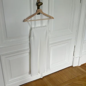 Vit klänning från Marks & Spencer - Elegant vit vintage klänning Den är ärmlös med tunna axelband och har en fin spetsdetalj längs kanten. Perfekt för sommarens fester eller en avslappnad dag ute. Klänningen är i storlek M men jag trycker den är ganska liten i storleken 