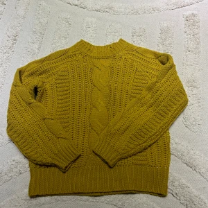 Gul stickad tröja från Pieces - Säljer en snygg gul stickad tröja från Pieces. Tröjan har ett flätmönster och ribbade muddar vid ärmslut och nederkant. Perfekt för kyliga dagar! Använd få gånger och är i mycket bra skick!