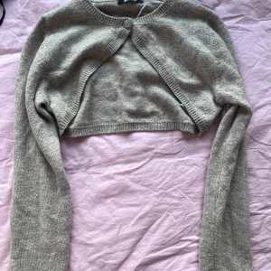 Beige bolerotopp från Gina Tricot - Säljer en stilren beige bolerotopp från Gina Tricot. Den är stickad med en knapp framtill och har långa ärmar. Perfekt för att lägga till en extra touch till din outfit. ALDRIG ANVÄNT 