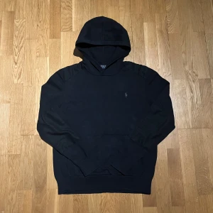 Svart hoodie från Polo Ralph Lauren - Säljer en stilren svart hoodie från Polo Ralph Lauren med det klassiska logotypbroderiet på bröstet. Tröjan har en bekväm passform och är perfekt för en avslappnad look. Liten fläck som förmodligen går bort i tvätten. Den har långa ärmar och en praktisk huva.