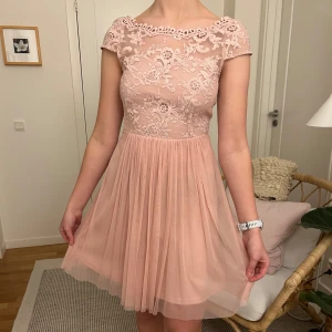 Rosa spetsklänning - Rosa klänning med spetsdetaljer och kort ärm. Den har en vacker öppen rygg med knappar och en luftig kjol. Använd 1 gång.